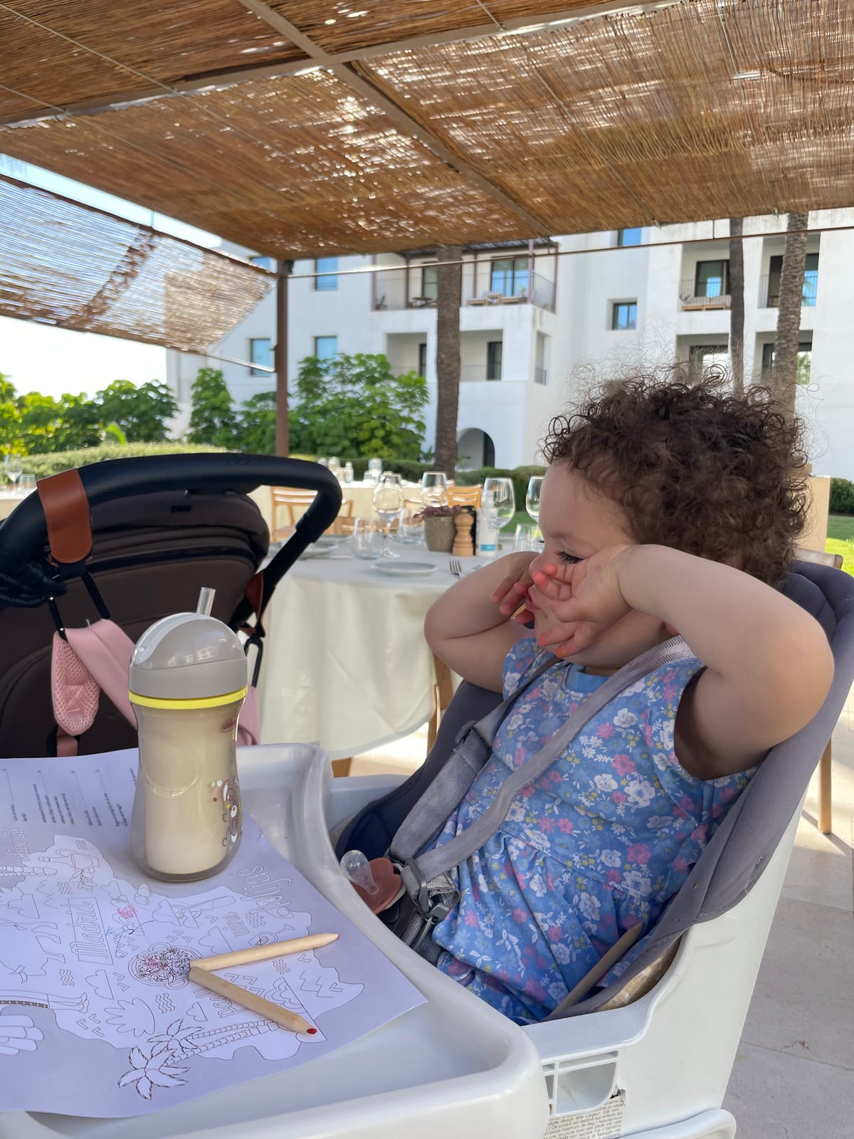 Toddler in a highchair at a shaded La Zambra restaurant terrace, with a colouring kids' menu and sippy cup on the tray.